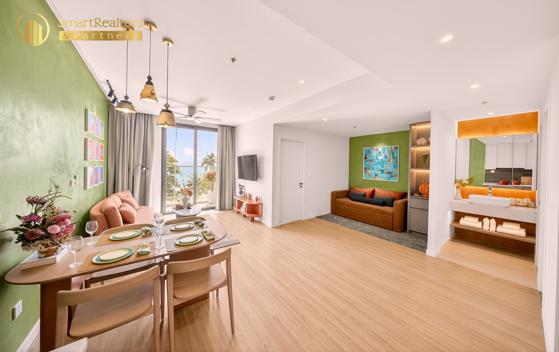 Không gian chung căn hộ mẫu 1PN: sofa, bàn ăn 4 chỗ, bếp mở và cửa kính ra ban công hướng biển