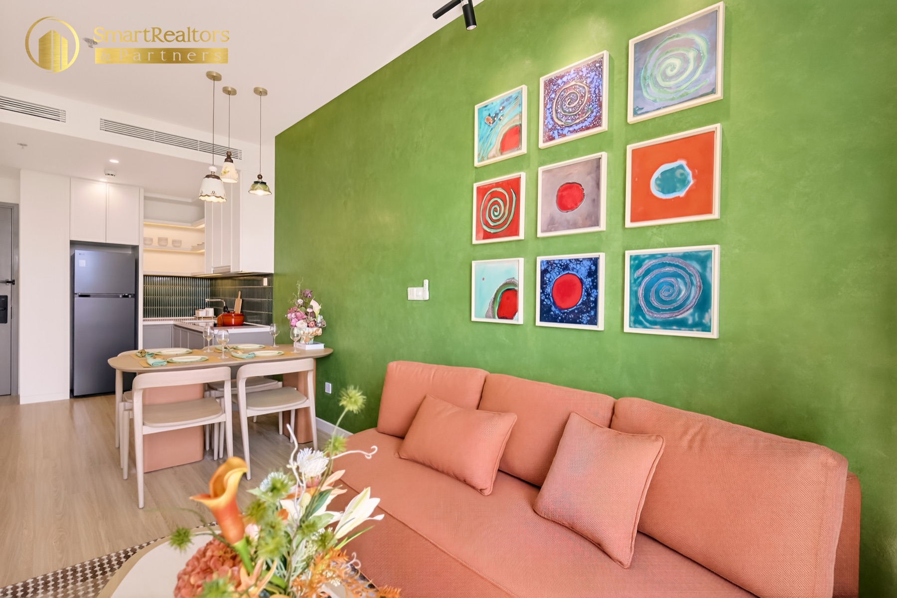 Sofa đặt dưới bộ tranh 9 khung, phía sau là khu bếp của căn hộ mẫu 1PN