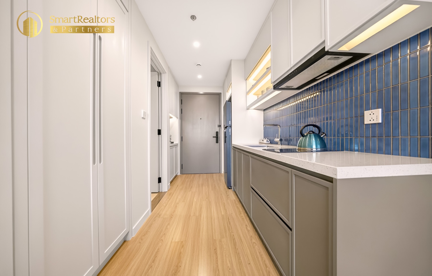 Bếp dọc hành lang căn hộ mẫu Studio với gạch ốp xanh và tủ bếp trắng